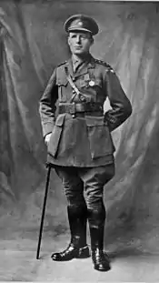 A full length portrait of a man in military uniform wearing two military medals and leaning on a swagger stick.