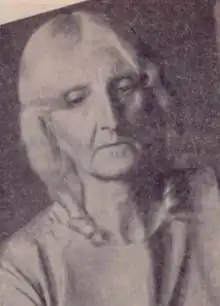 An older white woman with white hair, eyes cast downward