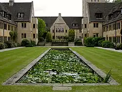 A long pool set in a grass lawn; stone buildings of two and three storeys on three sides