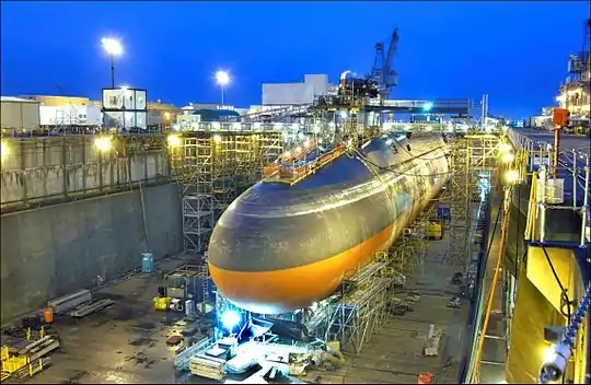 Black submarine with orange paint from cheatline down in drydock at nightfall