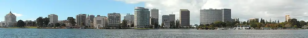 Daytime skyline of a city behind a lake, showing several tall skyscrapers in the middle of the image, with several low-rises on the left and trees on the right.