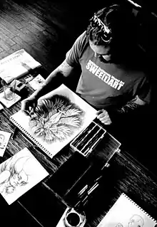 A black-and-white photo of a bearded man in an art studio