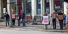 A group of seven people holding hand-lettered cardboard signs along a city street. The largest says "We are the 99%".