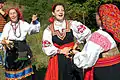 Russian women with treshchotka and Russian spoons in their hands. The two women on the right are wearing Sarafans.