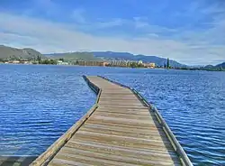 A walking bridge sits in the center of a bright lake with a business district in the background.