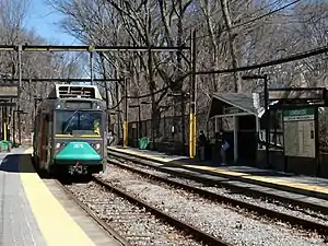 A light rail train at a station in a wooded area