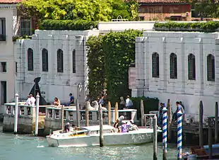 A large building on the edge of a canal with a boat and tourists in the foreground