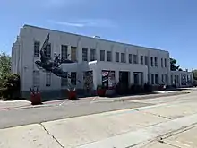 A gray art deco-style building with a black sparrow imprint on it.  Yucca plants in planters stand in front of the building.