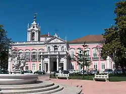 An ornate pink-and-white building in the baroque style is pictured from the front on a sunny day.