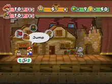  Mario with a goomba on a stage with cardboard, run-down buildings in the background. To the far right is Gus, a turtle-like creature, the current enemy they are fighting.