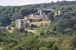 a wooded hillside, there is a large house, behind which are the ruins of a castle