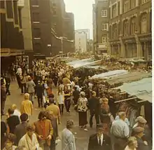 Colour photograph of a moderately crowded street, with stalls along one side.