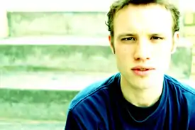 Gavin Castleton without ear piercings, sitting on stairs in a blue shirt.