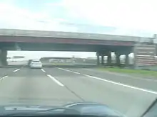 A large bridge hovering a 12-lane wide highway viewed from a car