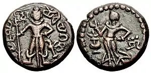 Yaudheya coin, imitative of Kushan coinage, 3rd-4th centuries CE. Obverse: Karttikeya standing facing, holding a spear with dvi (“two” in Brahmi) to the left of Karttikeya's head, peacock to lower right, Brahmi legend around: 𑀬𑁅𑀥𑁂𑀬 𑀕𑀦𑀲𑁆𑀬 𑀚𑀬 (yaudheya ganasya jaya, “Victory to the Yaudheya people”). Reverse: Devasena standing left, raising hand; flower vase to left, inverted nandipada to the right. of