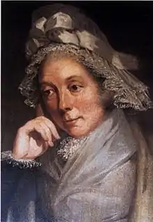 Quarter-length portrait of a woman in a brown and grey lace bonnet adorned with a bow and leaning on her right hand.