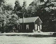 Single-story building in a field, flanked with trees