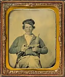 Sepia-toned photo of a young man holding a pistol.