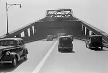 A grayscale photo of a four lane undivided road on a bridge