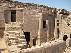 Rock cut tomb and pillars in brownish stone cliff under the blue sky of the Egyptian desert