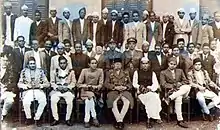 A group photograph of the Rana-Congress coalition cabinet of ministers. Bhadrakali Mishra is seated in the first row, wearing the traditional dhoti-kurta dress and the Gandhian cap. To the right of Mishra is Prime Minister Mohan Shamsher. Also in the photograph are other ministers and other senior administrative and security officials.