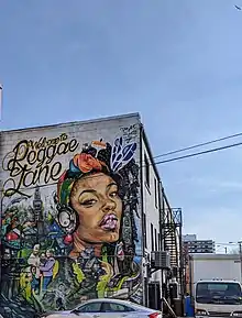 A mural depicting a young woman listening to music on headphones, a happy family and a train running through the streets of Toronto.