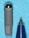 A standard  13 mm root form dental implant with pen beside it for size comparison