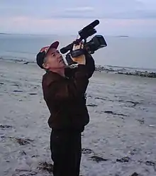 Photograph of Richard Dindo with camera, on beach at Plymouth, Massachusetts, USA, while directing the film Mars Dreamers.