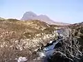 River Kirkaig where the river flows out of Fionn Loch with the imposing peak and most distinctive mountain of Suilven at 731 m, visible in the distance. It can't be seen from the bay, due to undergrowth and small undulating hills.