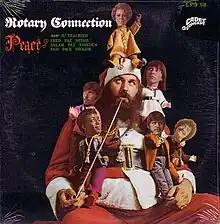 A photo of Santa seated with a pipe, surrounded by doll-sized members of the band