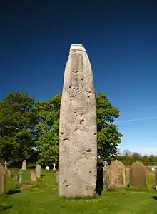 a cemetery over which towers a large standing stone with some sort of cap