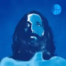 A blue-tinted headshot photograph of Sébastien Tellier, whom is bare-chested