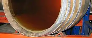 Colour photo showing the deposit of lees in barrel through a transparent bottom. Lees looks like a layer of mud a few millimetres thick of a creamy white colour. The light that passes through the wine is still cloudy suggesting that light should be placed against another background. The barrel rests on metal industrial shelving.