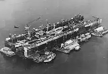 US Navy floating Dry Dock Number 4 in Seeadler Harbor 1945, surrounded by floating barges with workshops and a tugboat, repairing seaplane tender and Navy Liberty ship