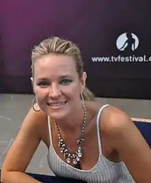 A women with blond hair, wearing an earring and a necklace also wearing a white top.