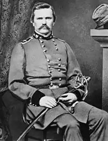 Black and white picture of a seated man with a moustache and no beard. He wears a gray military uniform with two stars on the collar.