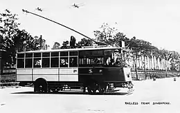 black and white photo showing sideview of an electric tram in Singapore; side is painted to show section for first and second class