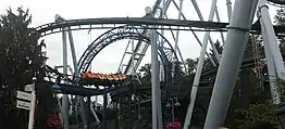 A view of the SooperDooperLooper's train as it traverses the layout. Pictured is one of the train's as it enters through the vertical loop. The track of the Great Bear inverted roller coaster hangs overhead before the loop, supported by white columns and purple track.