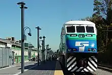 A passenger train parked at a train station's platform, which stretches into the background, interrupted by a series of lampposts and glass walls