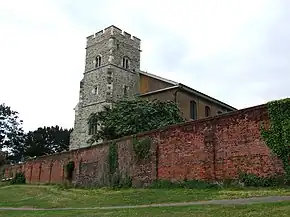 A grey stone tower rises above an ancient red brick boundary wall