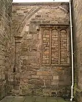 A dark painted wooden door, made of twelve vertical planks and dark iron hinges and nails, in an arched frame and wall of various light red and brown stones