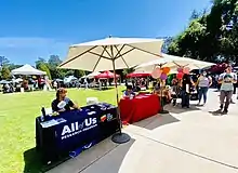 People in the Koret Plaza at Stanford University, with a man at a table with the All of Us service marks.