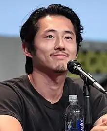 Yeun smiling behind a microphone