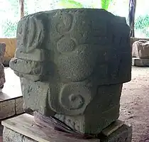 A finely carved sculpture in the form of a stylised bat's head with prominent nose seen from the front right. Decorations spiral outwards from above the eye and to the side of the mouth.