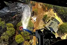 Photograph taken from a helicopter showing water being deployed on flames near a home