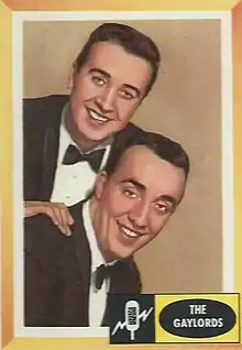 Two men in suits and bowties smile and pose, with Ronnie Gaylord leaning above Burt Holiday. There is a small yellow box in the bottom corner identifying them as The Gaylords.