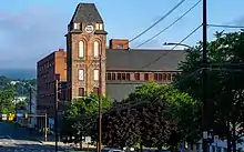 A brick tower with peaked roof on the right-hand side of a street in front of the camera. There are green hills in the background.