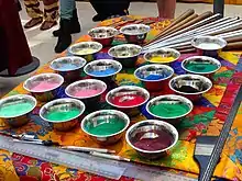 Bowls of colored sand on table alongside metal tools for applying sand