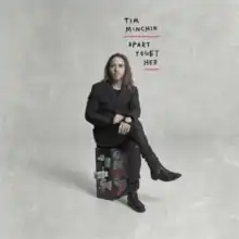 A man with long hair sits on a suitcase, with the words "Apart Together" written above him