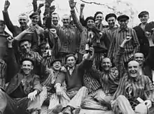 Dachau survivors toast their liberation as the man standing in center between the bottles wears a P triangle.